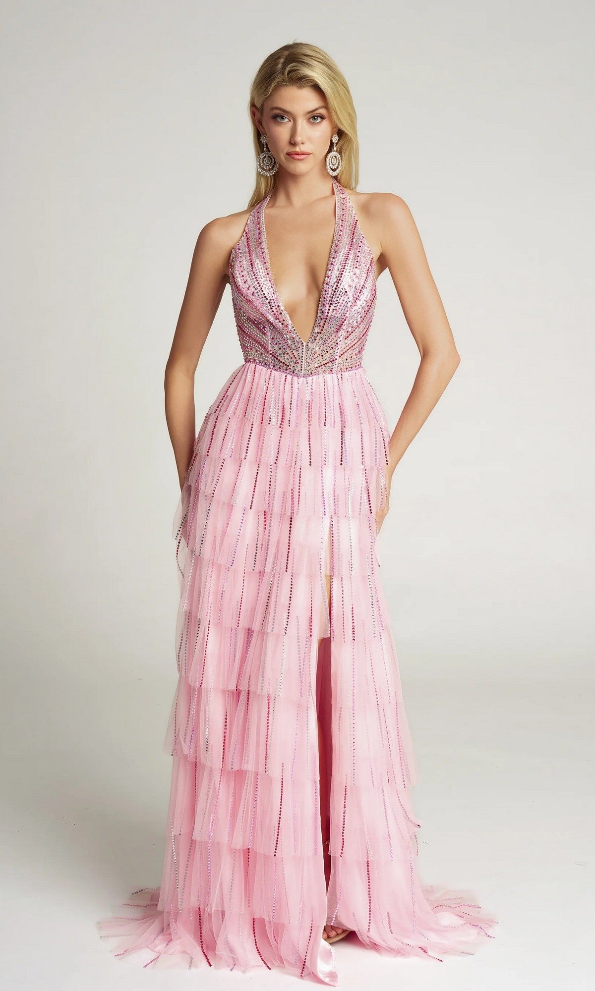 A woman stands against a plain light background wearing the Portia and Scarlett PS26117 long formal dress in pink, featuring a sleeveless deep V-neck, layered tulle skirt, and silver sequin embellishments.